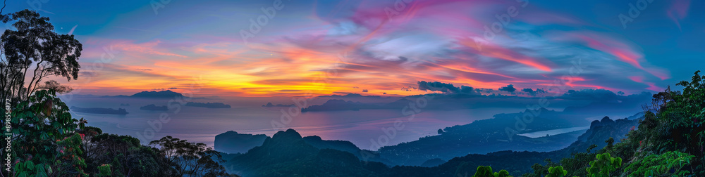 Fototapeta premium A panoramic view of the serene landscape at sunset, with mountains in the background and calm waters reflecting vibrant colors of orange, blue, green, yellow, pink, purple, and red
