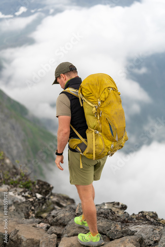 male backpacking hiker with yellow backpack climbing Romsdalseggen trail in Andalsnes Norway in summer with rocky mountains in the background photo