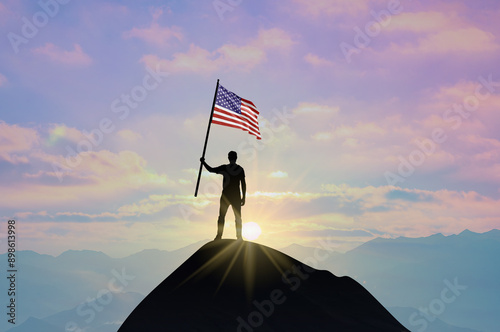 Waving flag of America at the top of a mountain summit against sunset or sunrise. American flag for Independence Day.