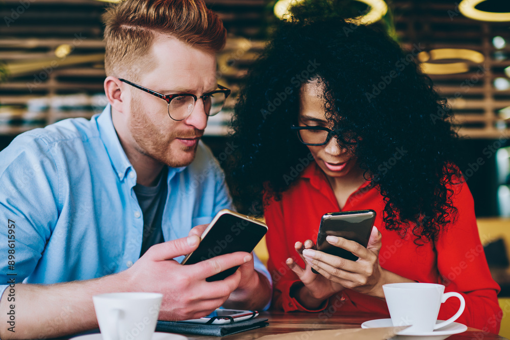 Two multicultural business partners sharing media files on smartphones using bluetooth connection.African american young woman showing caucasian male colleague application on mobile phone device