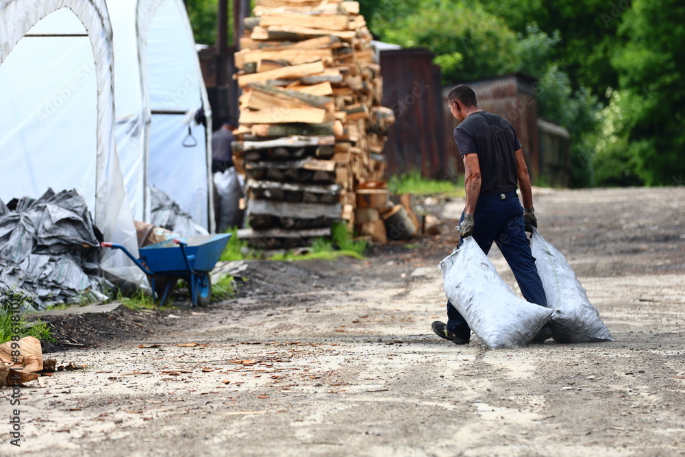 a worker working at a traditional charcoal burning plant in the Bieszczady Mountains pulls bags of prepared charcoal