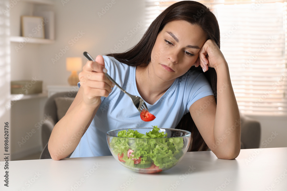 Eating disorder. Sad woman holding fork with tomato over bowl at table indoors Eating disorder. Sad woman holding fork with tomato over bowl at table indoors