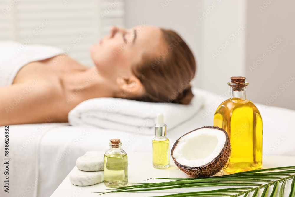 Aromatherapy. Woman relaxing on massage couch in spa salon, focus on bottles of essential oils, coconut and stones Aromatherapy. Woman relaxing on massage couch in spa salon, focus on bottles of essential oils, coconut and stones