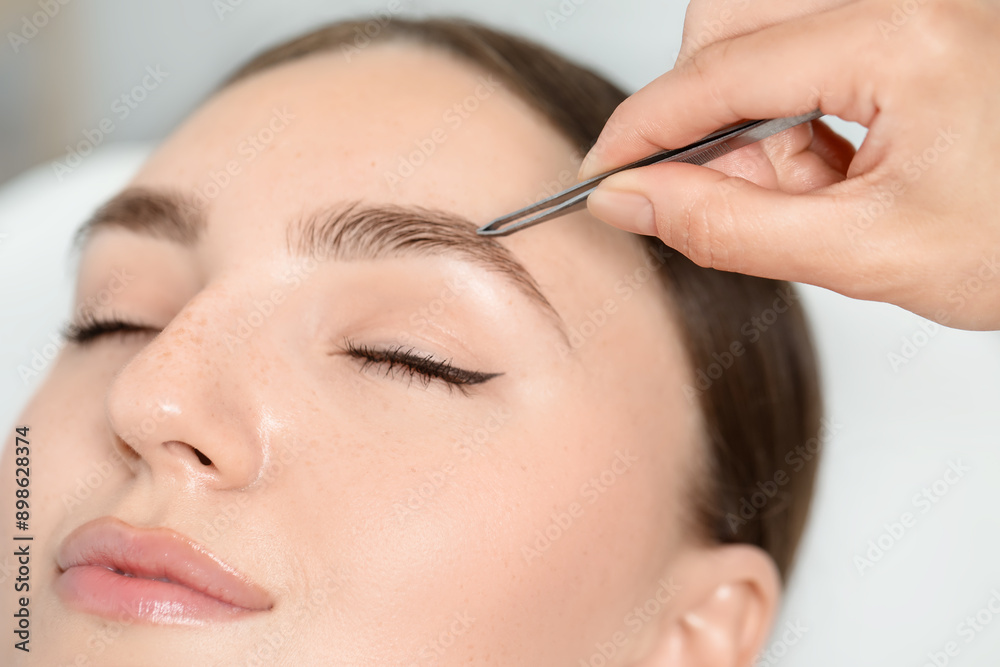 Beautician plucking young woman's eyebrow in beauty salon, closeup Beautician plucking young woman's eyebrow in beauty salon, closeup