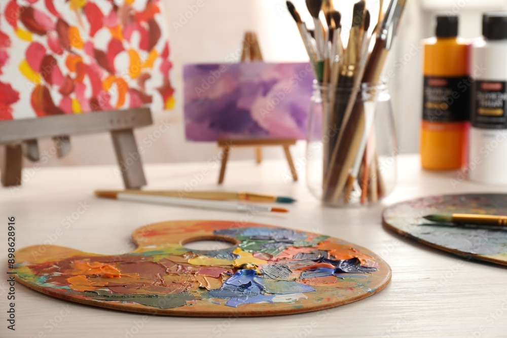 Artist's palette with mixed paints, brushes and small easels on wooden table indoors Artist's palette with mixed paints, brushes and small easels on wooden table indoors