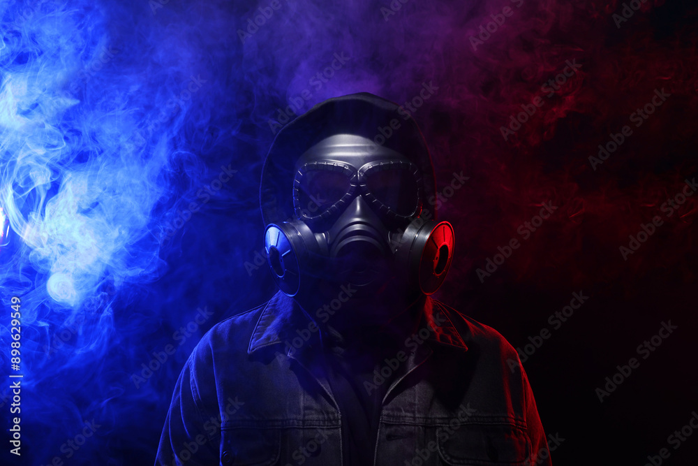 Man wearing gas mask in color lights and smoke on black background Man wearing gas mask in color lights and smoke on black background