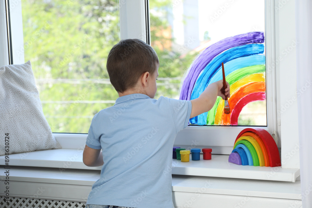 Little boy drawing rainbow on window indoors Little boy drawing rainbow on window indoors