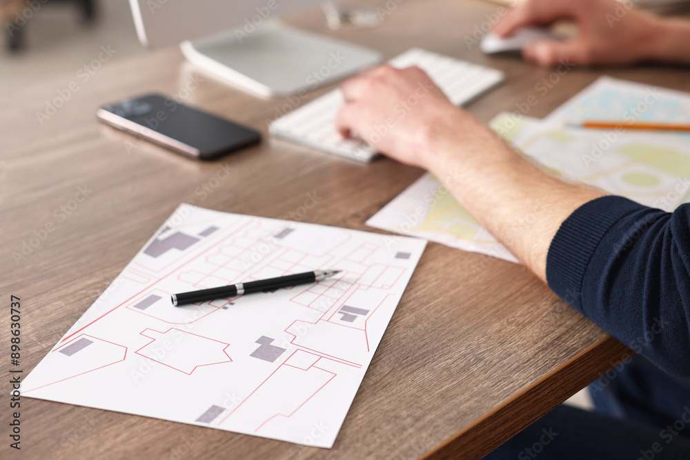 Cartographer working with cadastral maps at wooden table in office, closeup
