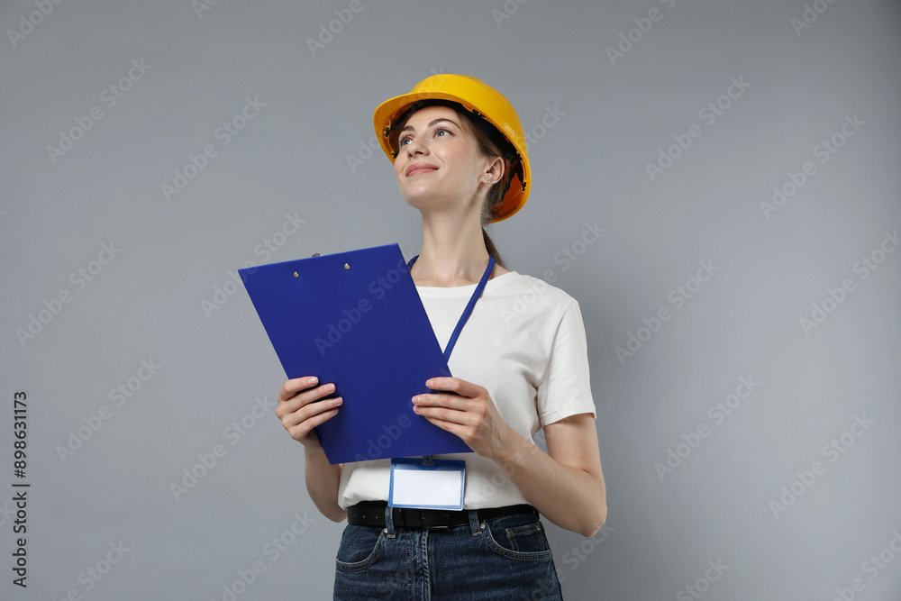 Engineer in hard hat with clipboard on grey background, low angle view Engineer in hard hat with clipboard on grey background, low angle view