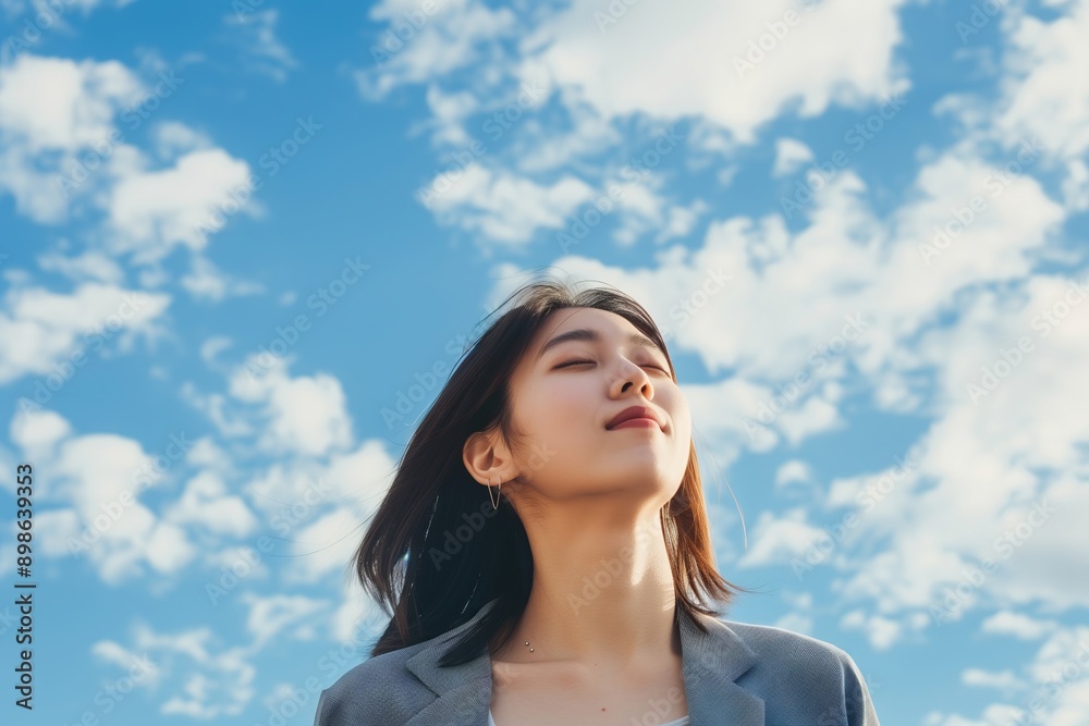 A woman is standing in the open air, looking up at the sky. She is wearing a gray jacket and she is enjoying the beautiful day A woman is standing in the open air, looking up at the sky. She is wearing a gray jacket and she is enjoying the beautiful day
