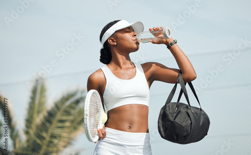 Fototapeta Naklejka Na Ścianę i Meble -  Tennis, water bottle and black woman on court, sports and fitness with nutrition, wellness and workout. African person, outdoor and athlete with liquid, racket and training with break, rest or health