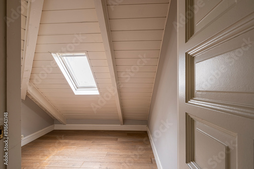 The photograph captures an empty attic room featuring a slanted roof and a small skylight window, creating a bright and cozy atmosphere ideal for various renovation ideas.