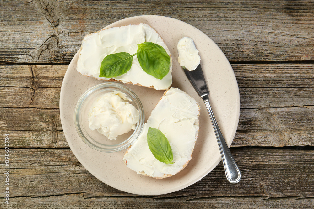 Delicious sandwiches with cream cheese and basil leaves on wooden table, top view Delicious sandwiches with cream cheese and basil leaves on wooden table, top view