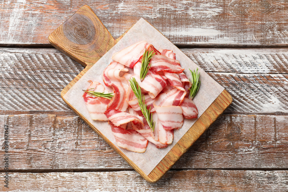Slices of raw bacon and rosemary on wooden table, top view Slices of raw bacon and rosemary on wooden table, top view
