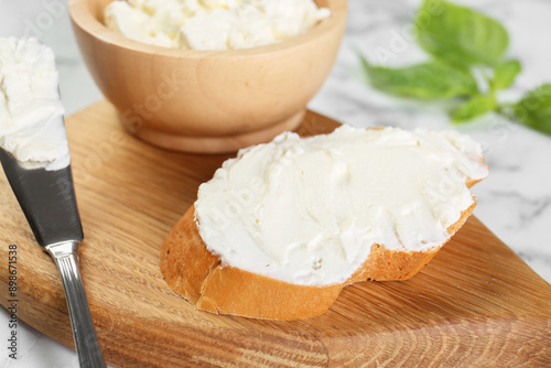 Piece of bread with cream cheese and knife on white marble table