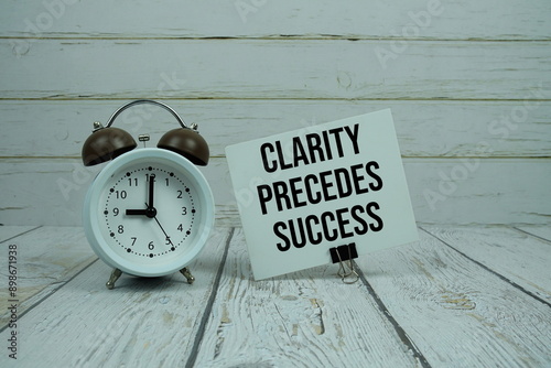 Clarity Precedes Success text on paper card with alarm clock on wooden background photo