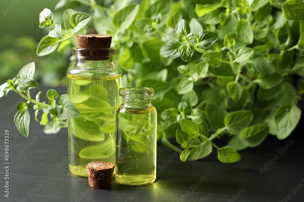 Essential oil in bottles and oregano twigs on dark textured table, closeup Essential oil in bottles and oregano twigs on dark textured table, closeup