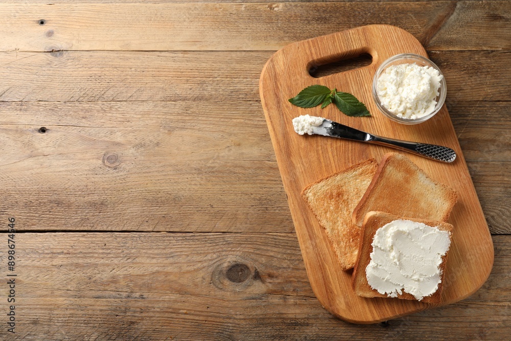 Delicious toasted bread slices with cream cheese, mint and knife on wooden table, top view. Space for text Delicious toasted bread slices with cream cheese, mint and knife on wooden table, top view. Space for text