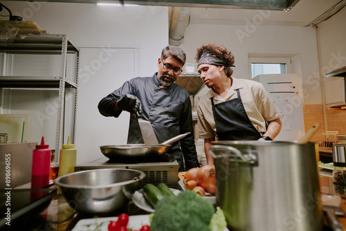 Chef and his sous chef discussing details of recipe while cooking together in professional restaurant kitchen