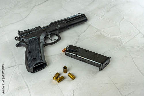 black pistol gun with magazine bullets and shells on empty white marble background