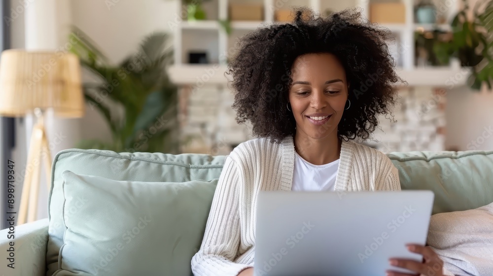 A content woman with curly hair smiles while using a laptop on her cozy couch at home, surrounded by comfortable furnishings, exemplifying a relaxed and blissful indoor environment. A content woman with curly hair smiles while using a laptop on her cozy couch at home, surrounded by comfortable furnishings, exemplifying a relaxed and blissful indoor environment.