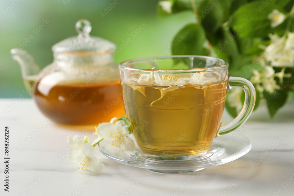 Aromatic jasmine tea in cup, flowers, teapot and green leaves on white marble table Aromatic jasmine tea in cup, flowers, teapot and green leaves on white marble table