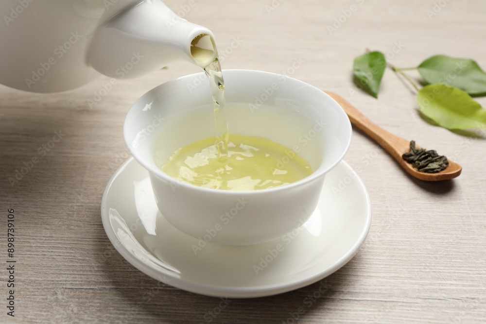Pouring refreshing green tea into cup at wooden table, closeup Pouring refreshing green tea into cup at wooden table, closeup