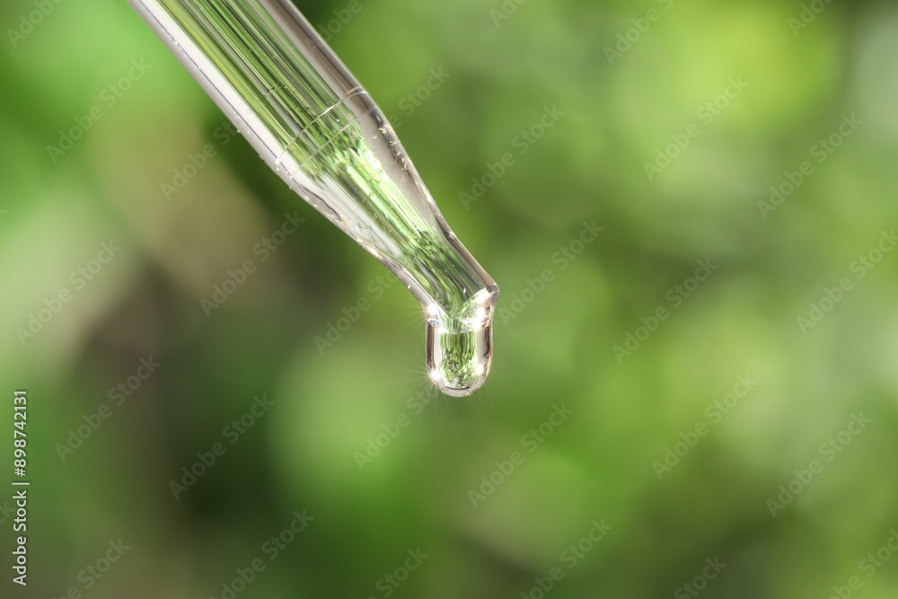 Essential oil dripping from pipette on blurred background, closeup Essential oil dripping from pipette on blurred background, closeup