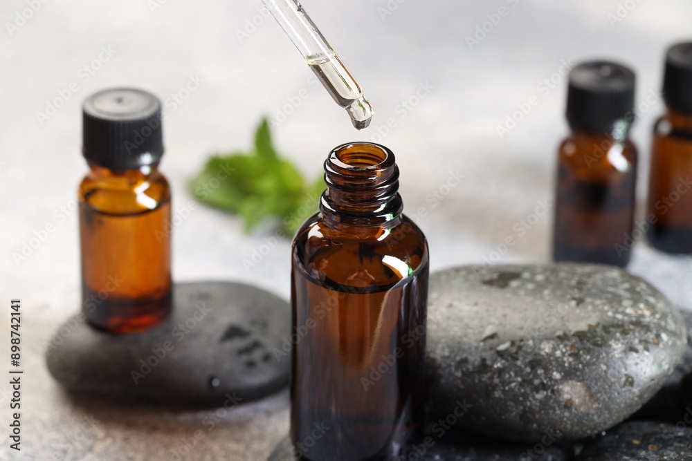Essential oil dripping from pipette into bottle on table, closeup Essential oil dripping from pipette into bottle on table, closeup