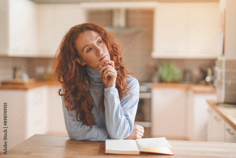 Redhead Woman Thinking in Kitchen While Sitting at Table With Note Book Redhead Woman Thinking in Kitchen While Sitting at Table With Note Book