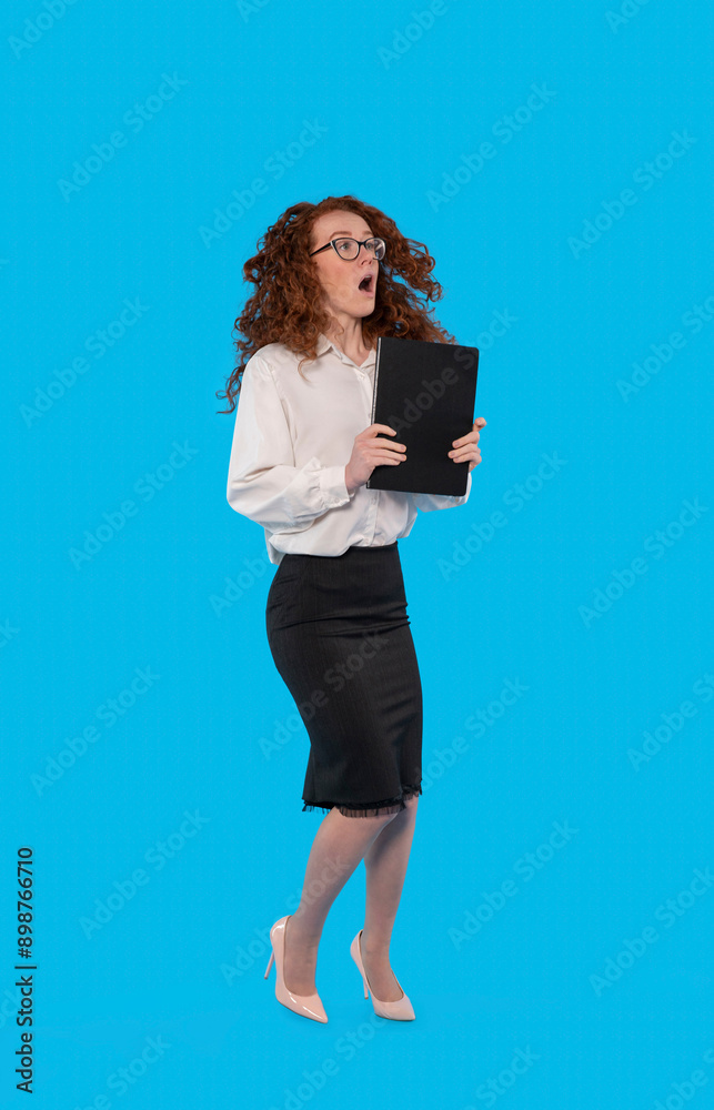 Surprised Woman With Red Hair Holding Black Folder Against Blue Background Surprised Woman With Red Hair Holding Black Folder Against Blue Background