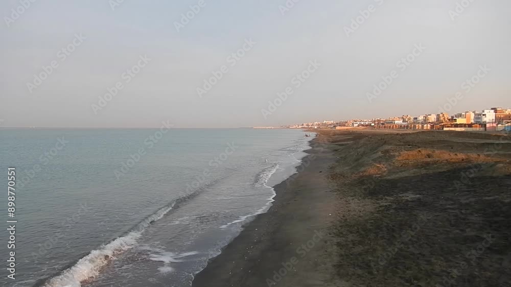 Mediterranean Sea with small waves, horizon, sky, coast with sandy beach and buildings lit orange by rising sun at dawn in Rome Ostia in Italy - with sound of waves. Topics: seaside resort, morning Mediterranean Sea with small waves, horizon, sky, coast with sandy beach and buildings lit orange by rising sun at dawn in Rome Ostia in Italy - with sound of waves. Topics: seaside resort, morning