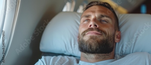  A man reclines in a hospital bed, eyes shut, head supported by a pillow's back