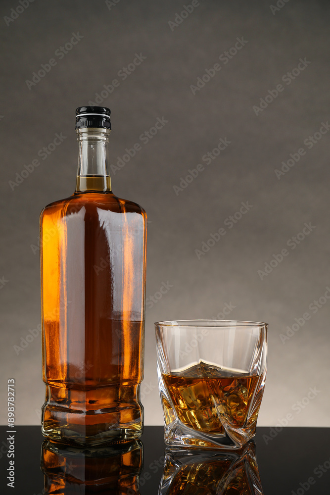 Bottle and glass with whiskey on table against gray background