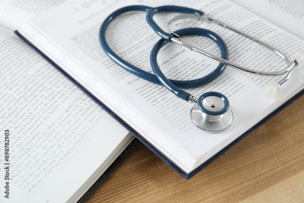 One new medical stethoscope and books on wooden table, closeup