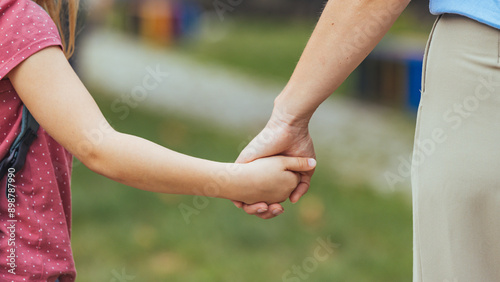Billede på lærred Close view highlights a young girl in a polka-dot top, gripping her mother's hand, wearing a pale blouse, as they walk together outside, with the daughter's backpack suggesting a school-bound journey