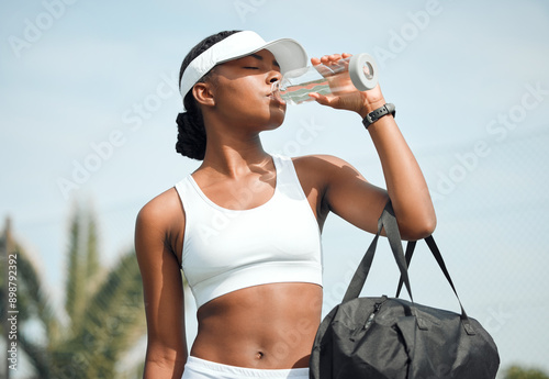 Fototapeta Naklejka Na Ścianę i Meble -  Tennis, drinking water and black woman on court, sports and fitness with nutrition, wellness and workout. African person, outdoor and athlete with bottle racket and training with break and healthy