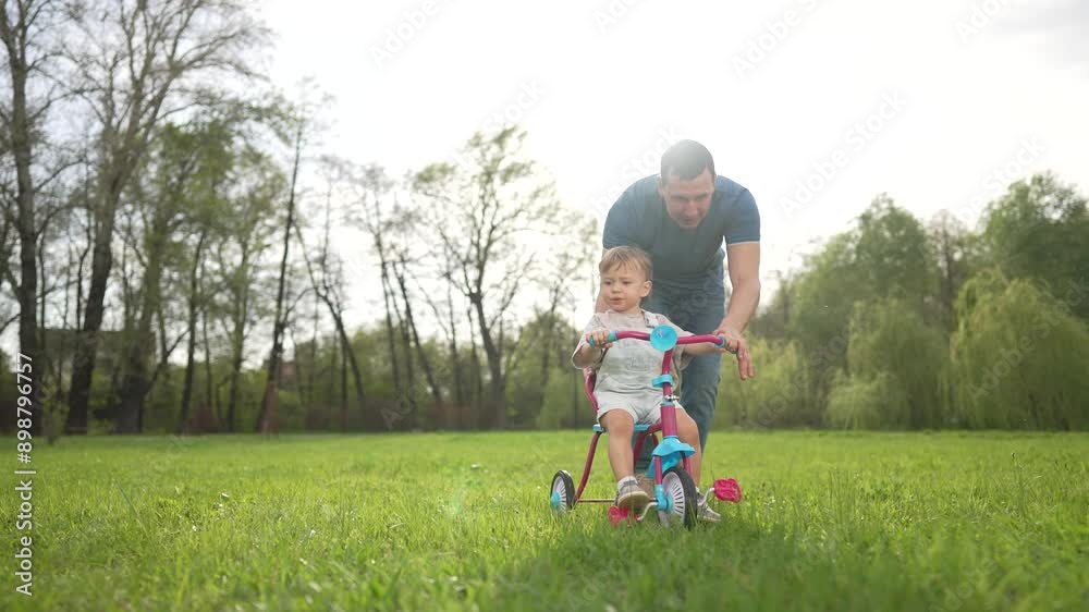 Father helps toddler ride tricycle park. Family teaching toddler to ride outdoors. Happy toddler learns ride tricycle with father help. Joyful family playing together. Toddler help ride fun outdoors. Father helps toddler ride tricycle park. Family teaching toddler to ride outdoors. Happy toddler learns ride tricycle with father help. Joyful family playing together. Toddler help ride fun outdoors.