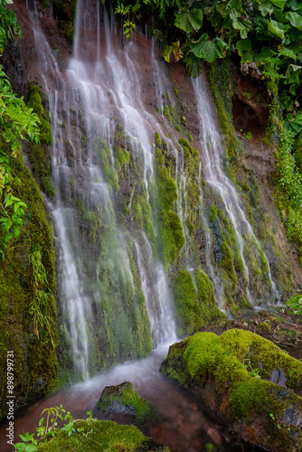 A wall of waterfalls on a green moss-covered slope of a volcano, Iturup Island