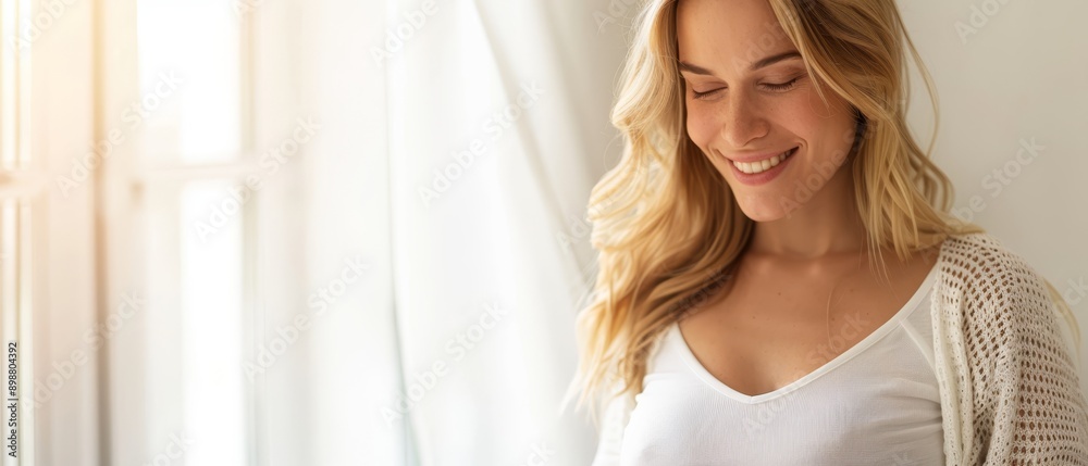 A woman smiles, with eyes closed, while holding a cardigan over her shoulder, in front of an open window A woman smiles, with eyes closed, while holding a cardigan over her shoulder, in front of an open window