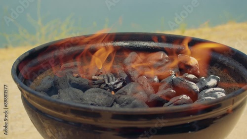 Close-up view of a brazier with burning charcoal standing near lake. Fire burns in a round black blazier, lake waters are visible in the background. photo