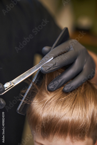 Close-up view experienced hairdresser cutting ends of hair to little boy