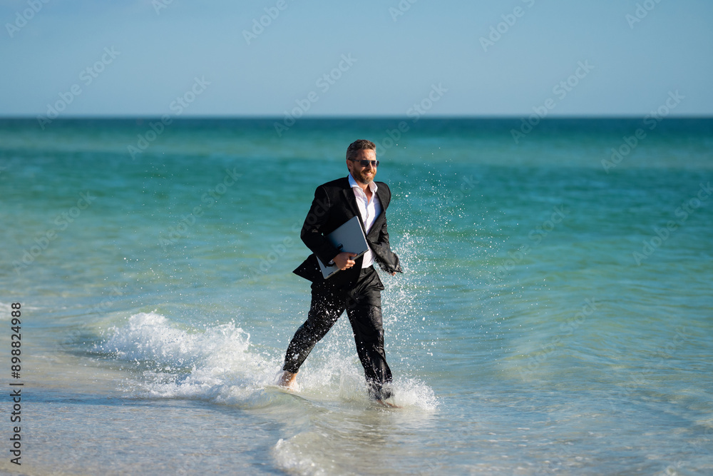 Fast business. Freelancer run outdoor. Businessman in suit with laptop running in sea water. Travel and tourism in sea. Crazy employee with laptop running in sea. Business man run on summer vacation. Fast business. Freelancer run outdoor. Businessman in suit with laptop running in sea water. Travel and tourism in sea. Crazy employee with laptop running in sea. Business man run on summer vacation.