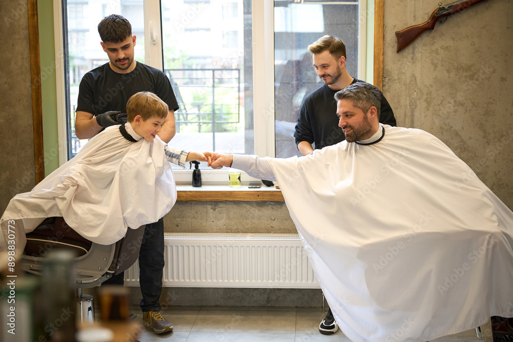 Obraz premium Little boy giving fist bump to father who sitting in barber chair