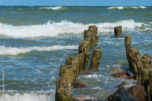 Old breakwater made of slanted wooden logs on the seashore. There are surf waves with white foam. Background. Texture. photo