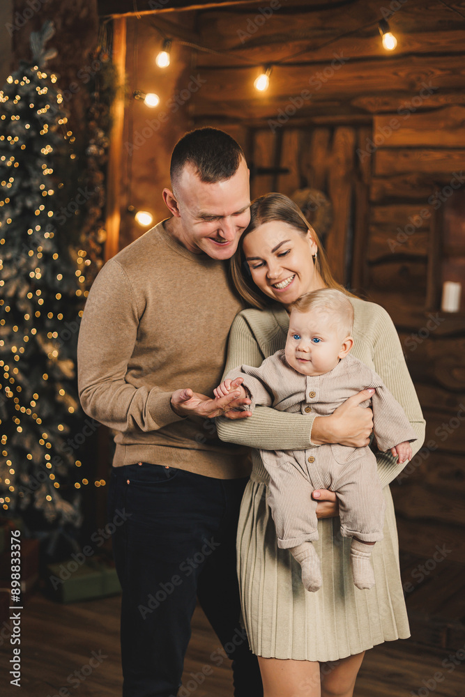 A happy family couple with a child in their arms on the background of a Christmas tree. New Year with a baby. Family New Year's atmosphere. A happy family couple with a child in their arms on the background of a Christmas tree. New Year with a baby. Family New Year's atmosphere.