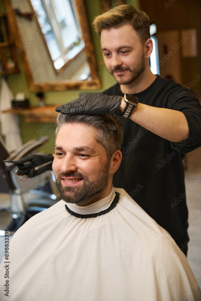 Young hairstylist combing hair and cutting ends to adult smiling man Young hairstylist combing hair and cutting ends to adult smiling man