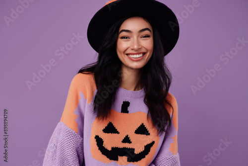 cheerful young woman in purple knitted sweater with  jack o lanter pumpkin design wearing black hat for halloween photo