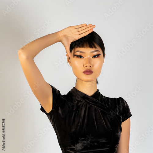 Femme élégante avec une frange noire et un T-shirt pose sur un fond blanc, elle fait un signe de salut de la main inspiré du geste militaire photo