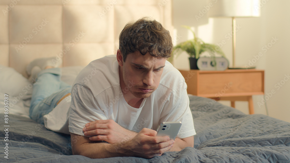 Caucasian unhappy man lying on bed user smartphone mobile phone cellphone frowning breakdown spam male guy crash app device worry banking confused displeased social media lost connection network fraud Caucasian unhappy man lying on bed user smartphone mobile phone cellphone frowning breakdown spam male guy crash app device worry banking confused displeased social media lost connection network fraud